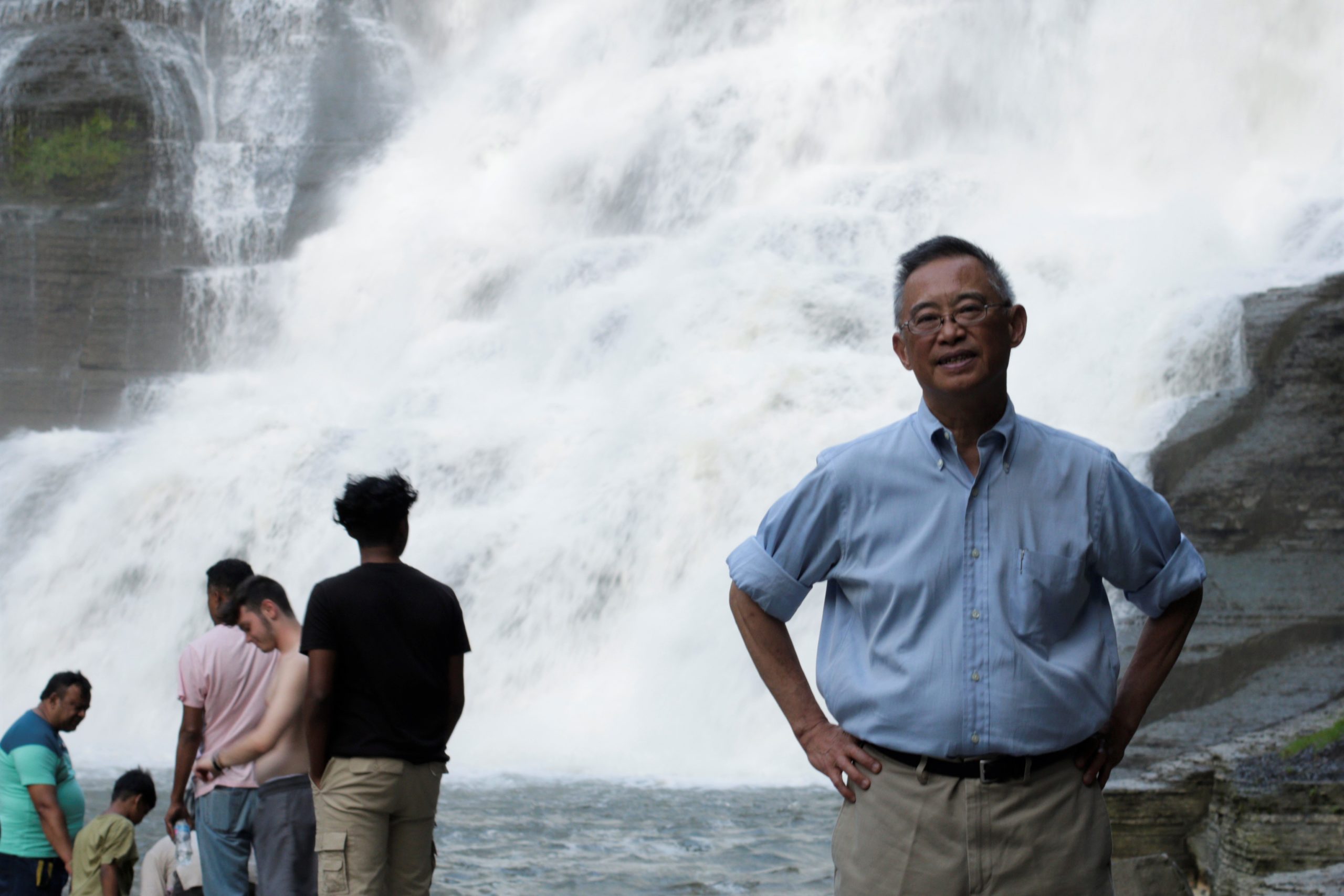 Walter Hang has been calling for a complete remediation of the lead pollution at the Ithaca Falls Natural Area for almost 20 years now. Behind him, people enjoy the falls, stepping into the water. They are seemingly unperturbed by, or unaware of, the lead pollution at the site. (Jimmy Jordan / WRFI)