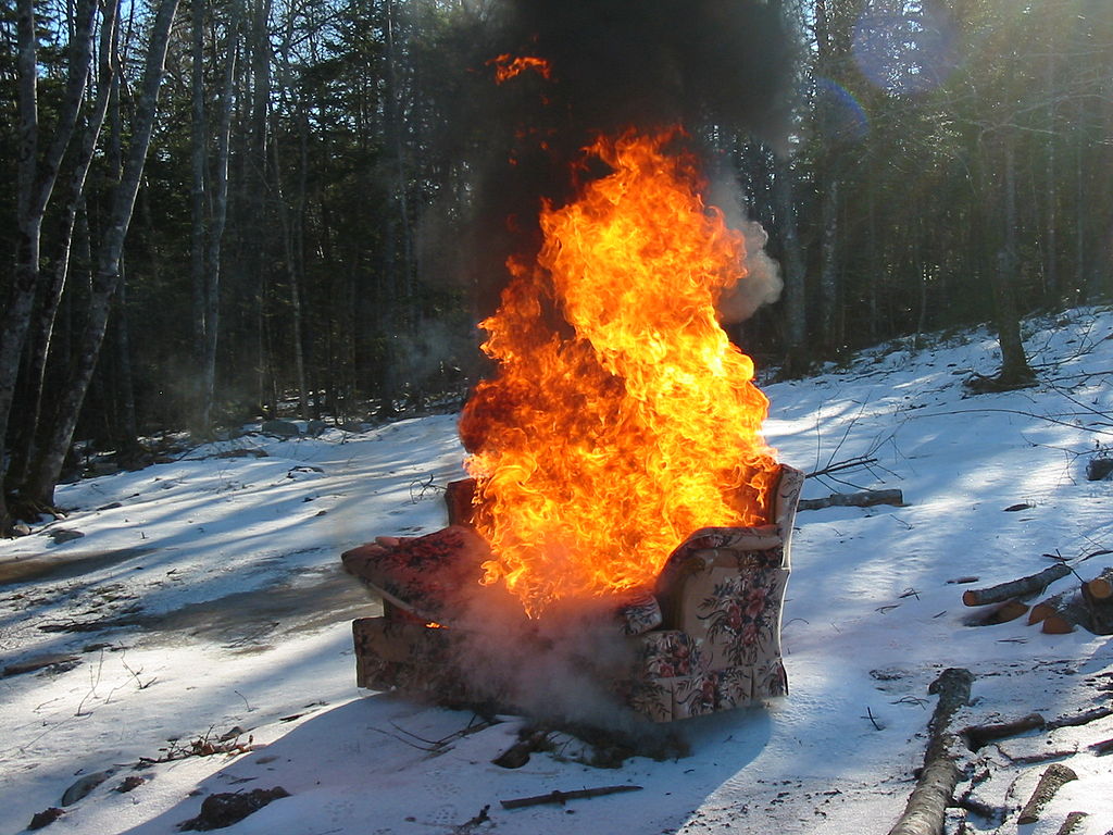Burning couch with floral pattern in woods with snow covered ground.