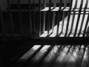 Black and white photo of prison bars and floor with stark light coming from within.