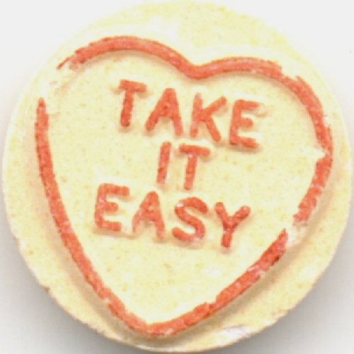 Image of a light yellow valentines candy that reads "Take it Easy" in red text inside a red heart